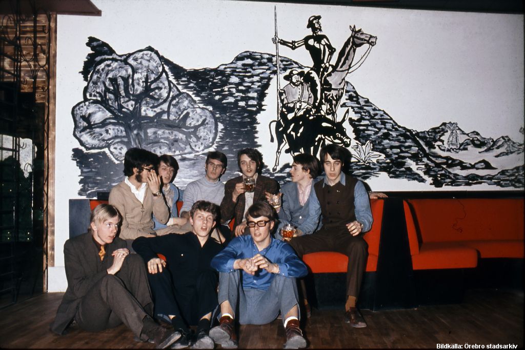 En grupp unga män sitter i och framför en röd soffa.