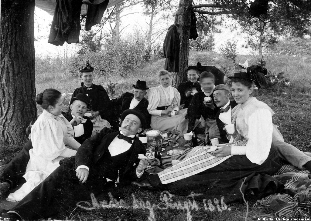 En grupp människor samlad på en filt med mat och dryck ute i naturen. 