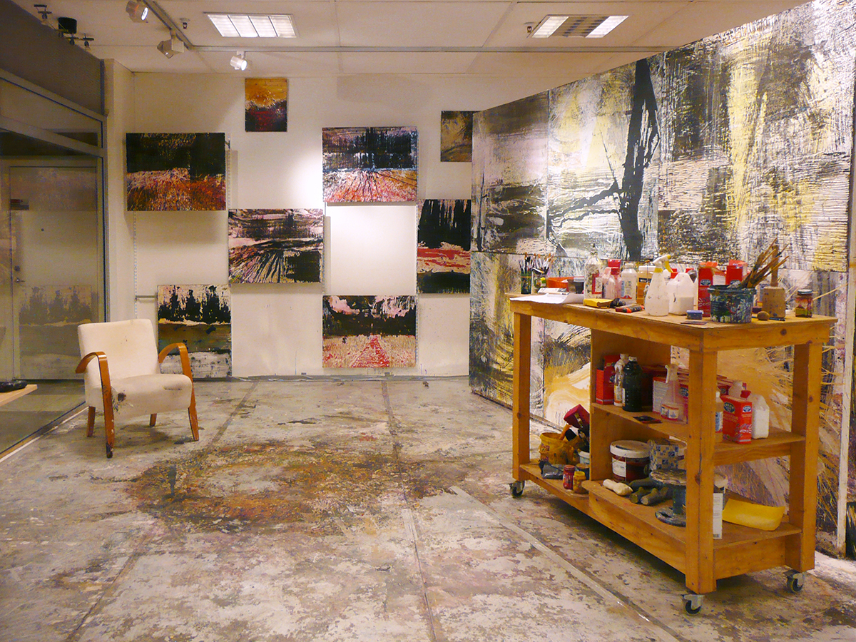 En uppbyggd studio med en fåtölj samt en arbetsbänk och hela väggarna är täckta med konst. 