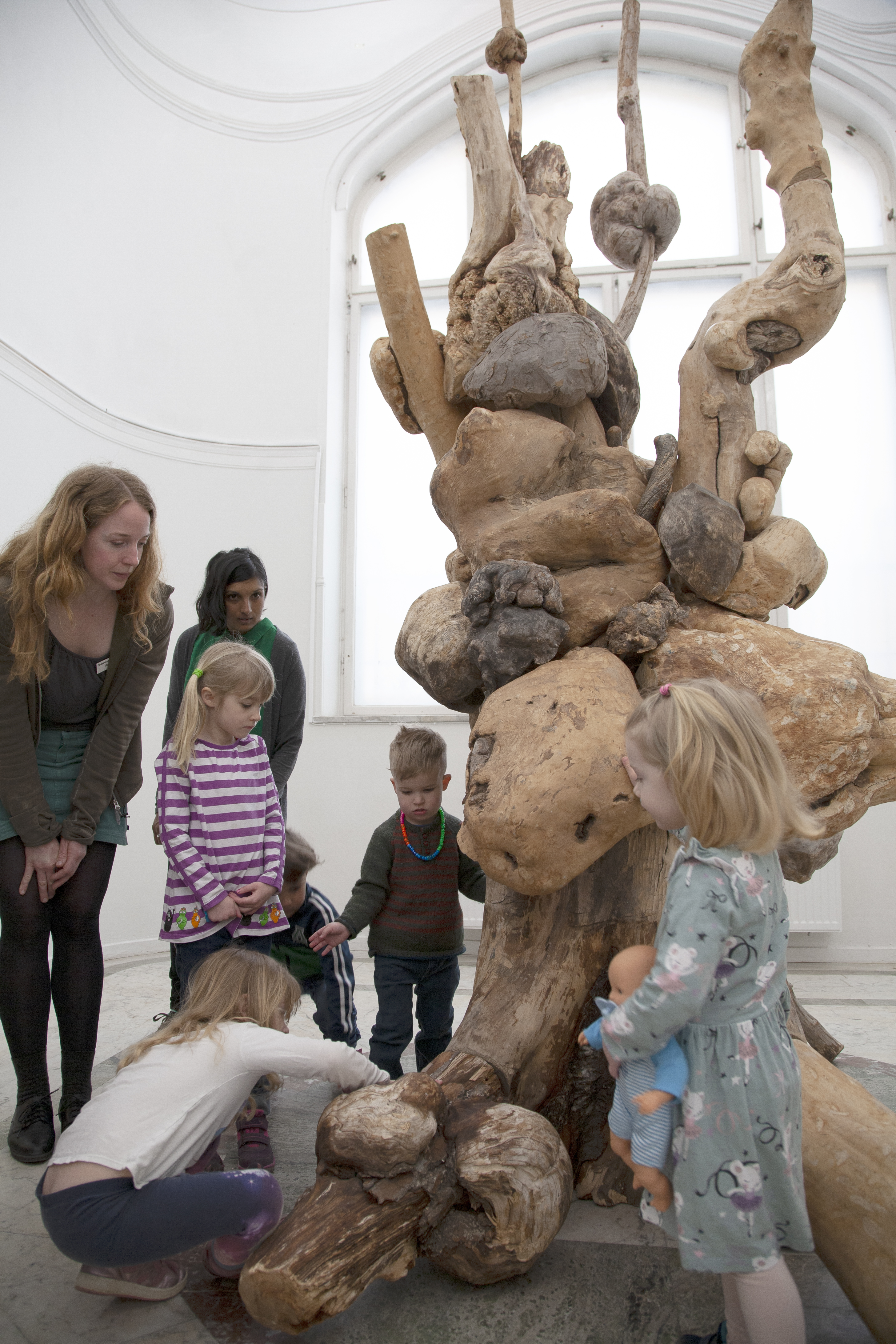 Barn och vuxna utforskar ett träkonstverk i form av ett knotigt trä